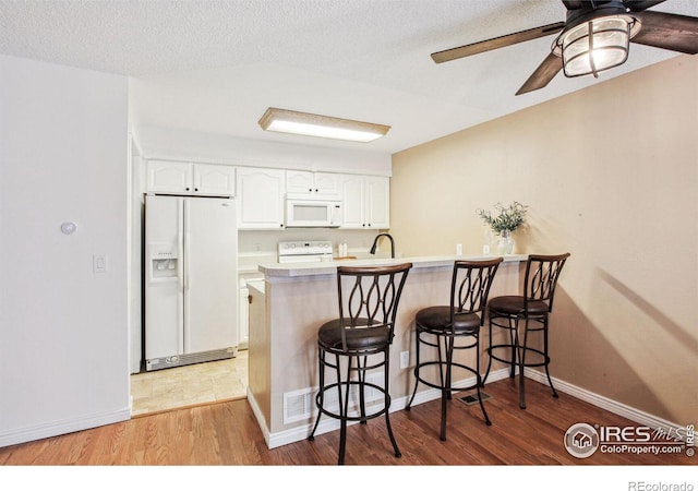 kitchen with white appliances, kitchen peninsula, ceiling fan, a breakfast bar area, and white cabinets