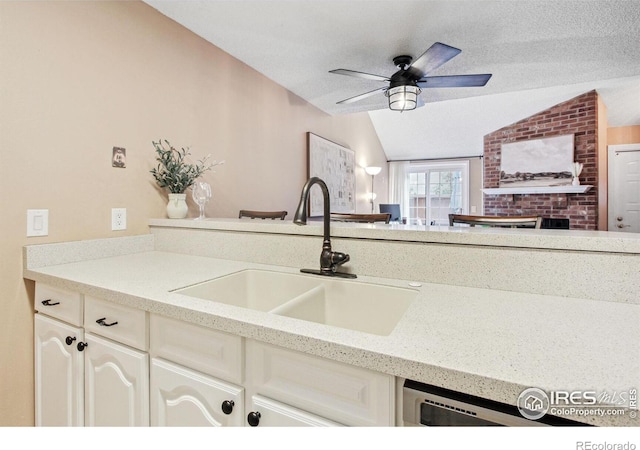 kitchen with a fireplace, a textured ceiling, sink, ceiling fan, and vaulted ceiling