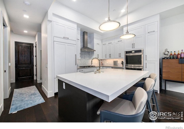 kitchen with dark hardwood / wood-style flooring, white cabinets, hanging light fixtures, tasteful backsplash, and wall chimney range hood