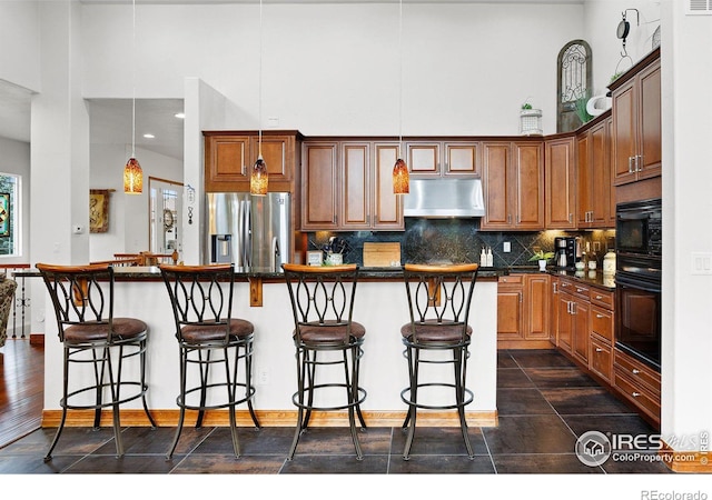 kitchen with black appliances, an island with sink, decorative light fixtures, and a kitchen breakfast bar