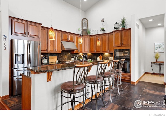 kitchen featuring a kitchen island with sink, dark tile patterned flooring, backsplash, black appliances, and hanging light fixtures