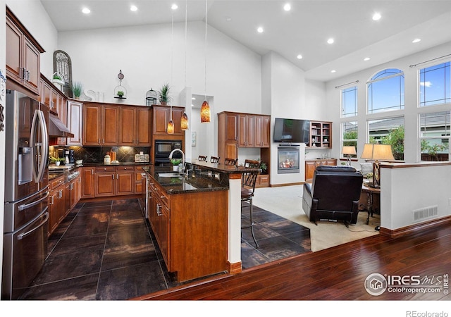 kitchen with high vaulted ceiling, stainless steel fridge, sink, a breakfast bar area, and a center island with sink