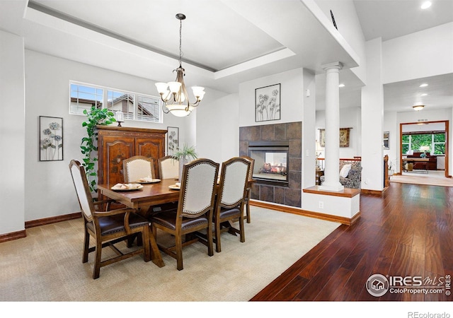 dining room with hardwood / wood-style floors, a chandelier, decorative columns, a tile fireplace, and a tray ceiling