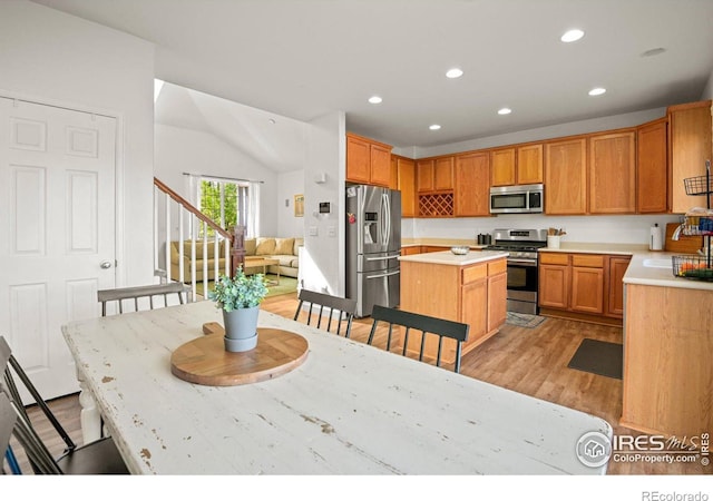 kitchen featuring light wood-type flooring, a kitchen island, sink, appliances with stainless steel finishes, and lofted ceiling