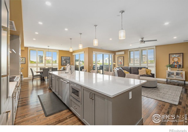 kitchen with dark wood-type flooring, stainless steel appliances, a center island with sink, and ceiling fan