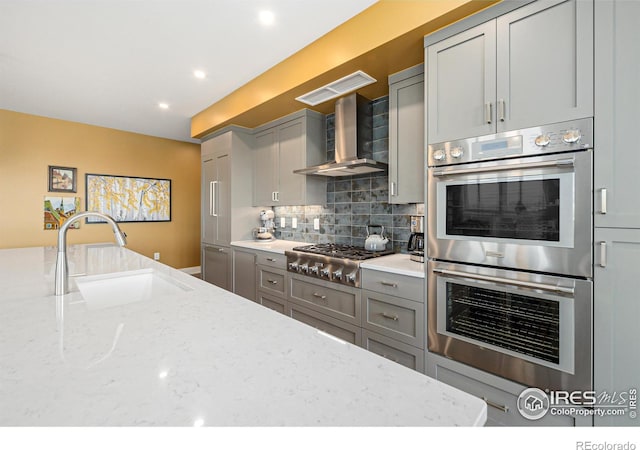 kitchen with wall chimney range hood, light stone counters, stainless steel appliances, and sink