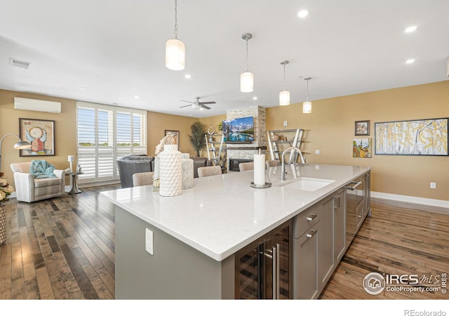 kitchen with dark hardwood / wood-style floors, a kitchen island with sink, sink, and a stone fireplace