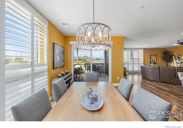 dining space with ceiling fan with notable chandelier and hardwood / wood-style floors