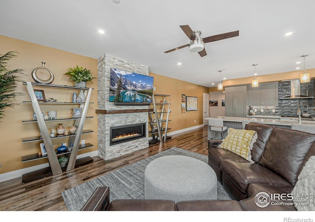 living room with dark wood-type flooring, ceiling fan, sink, and a fireplace