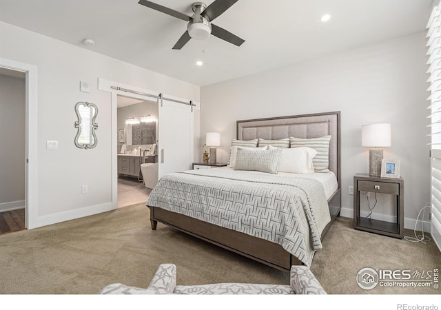 bedroom with a barn door, ensuite bath, light colored carpet, and ceiling fan