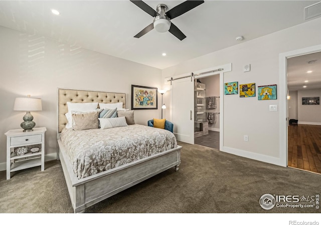 bedroom featuring dark carpet, connected bathroom, ceiling fan, and a barn door