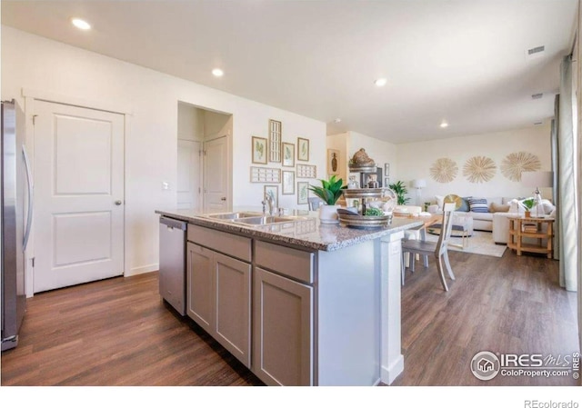 kitchen with a kitchen island with sink, stainless steel appliances, dark hardwood / wood-style flooring, light stone counters, and sink