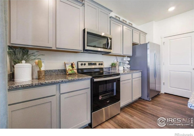 kitchen featuring stainless steel appliances, gray cabinetry, dark hardwood / wood-style flooring, and dark stone counters