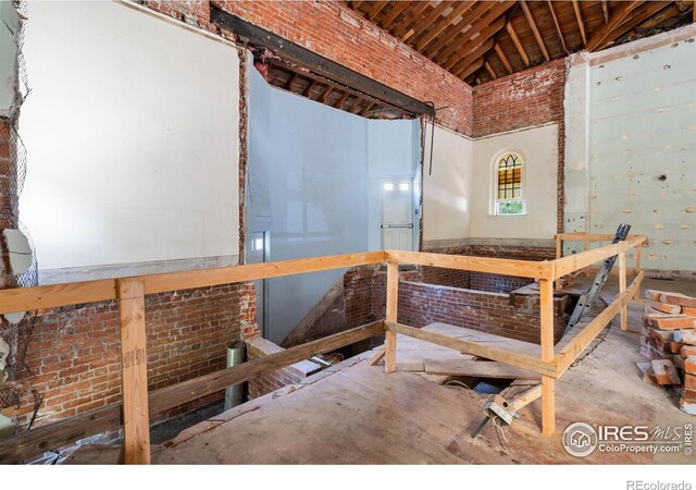 miscellaneous room with high vaulted ceiling, brick wall, and concrete floors