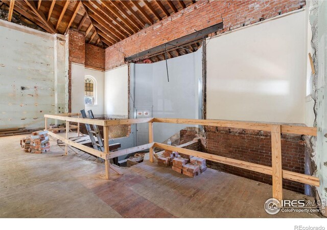 miscellaneous room with concrete flooring, high vaulted ceiling, and brick wall