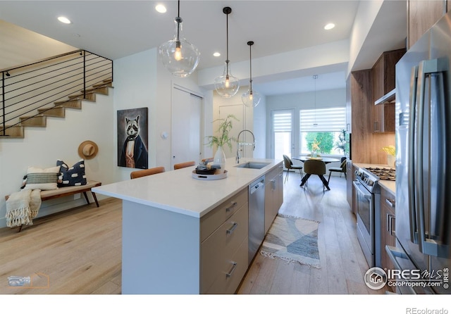 kitchen with pendant lighting, light hardwood / wood-style flooring, a kitchen island with sink, stainless steel appliances, and sink