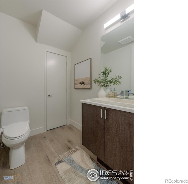 bathroom with lofted ceiling, wood-type flooring, toilet, and vanity