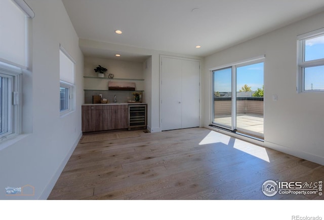 unfurnished living room featuring a healthy amount of sunlight, beverage cooler, and light wood-type flooring