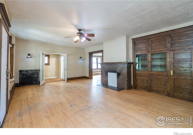 unfurnished living room featuring a fireplace, light hardwood / wood-style flooring, ceiling fan, and radiator heating unit