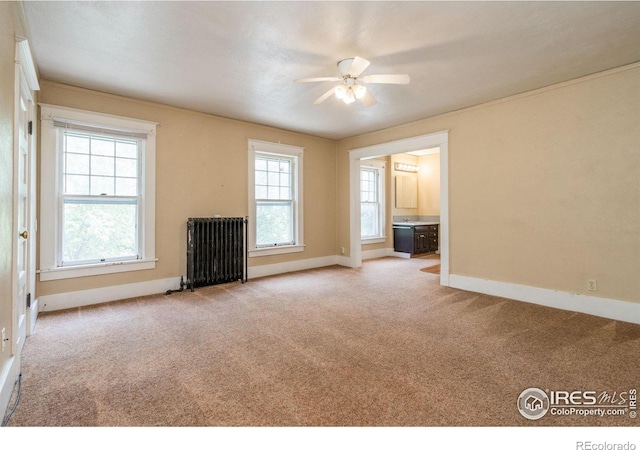 unfurnished living room featuring plenty of natural light, ceiling fan, radiator heating unit, and light carpet