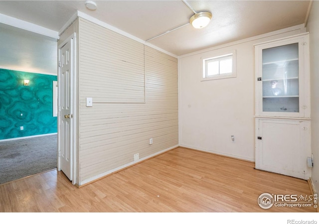 unfurnished room featuring light wood-type flooring, wood walls, and ornamental molding