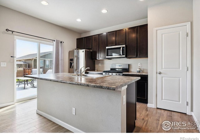 kitchen with appliances with stainless steel finishes, light hardwood / wood-style flooring, sink, and a center island with sink