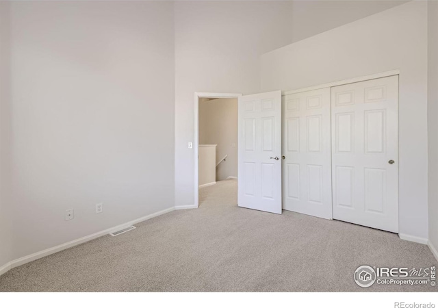 unfurnished bedroom featuring light colored carpet, a closet, and a towering ceiling