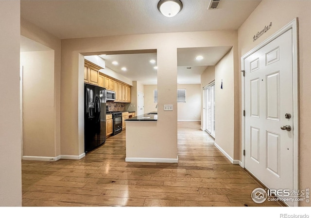 kitchen featuring light wood-type flooring, backsplash, black appliances, light brown cabinetry, and sink