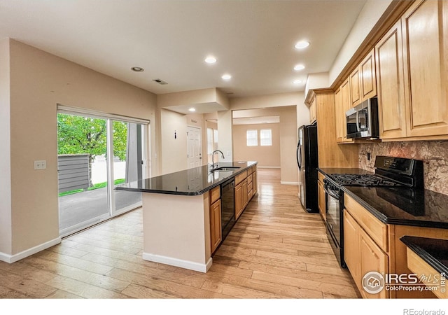 kitchen with light wood-type flooring, black appliances, a center island with sink, and sink