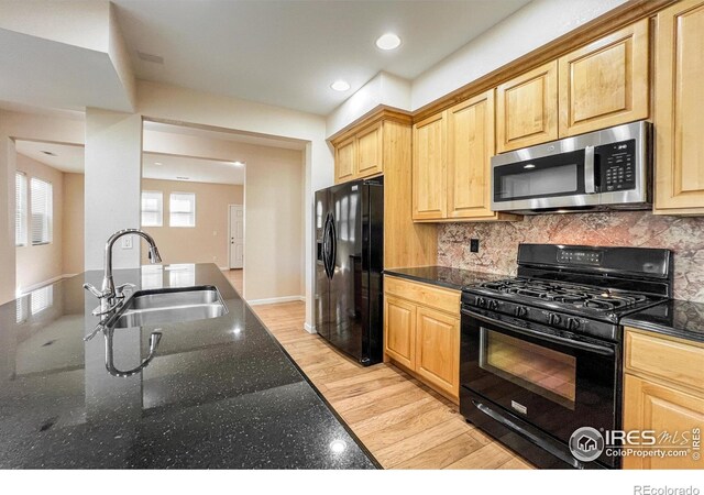 kitchen featuring black appliances, light hardwood / wood-style flooring, tasteful backsplash, sink, and dark stone counters