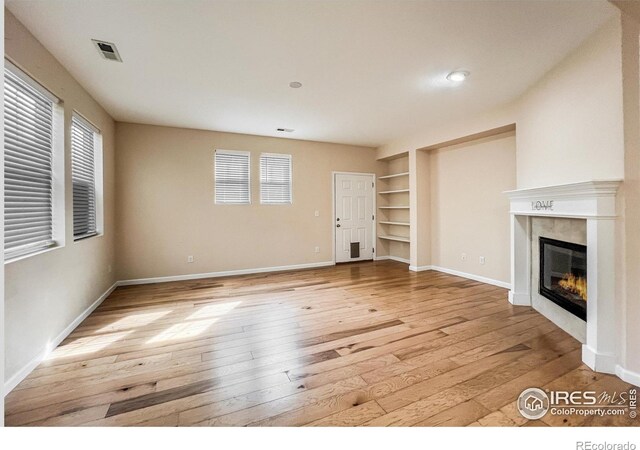 unfurnished living room with built in shelves, a premium fireplace, and light wood-type flooring