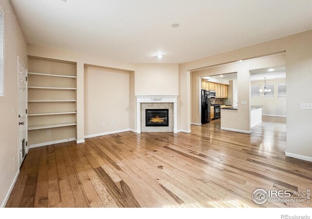 unfurnished living room with a tiled fireplace, hardwood / wood-style floors, and a notable chandelier