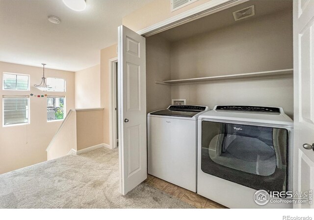 laundry room with washing machine and clothes dryer, light colored carpet, and a notable chandelier