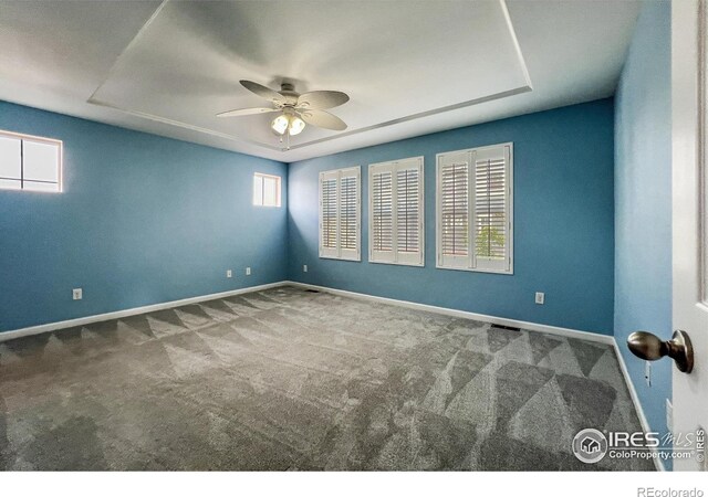 carpeted spare room featuring a tray ceiling, a wealth of natural light, and ceiling fan