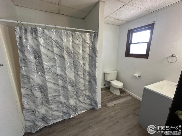 bathroom with toilet, a drop ceiling, vanity, curtained shower, and wood-type flooring