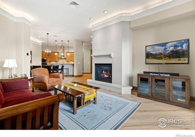 living room featuring ornamental molding, a tile fireplace, and light hardwood / wood-style floors