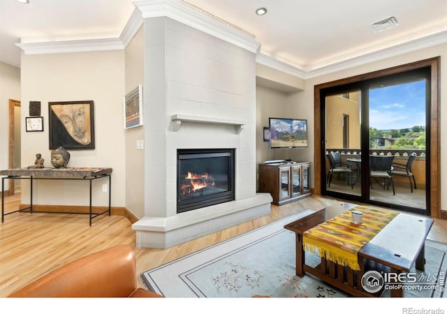 living room featuring wood-type flooring, a fireplace, and crown molding