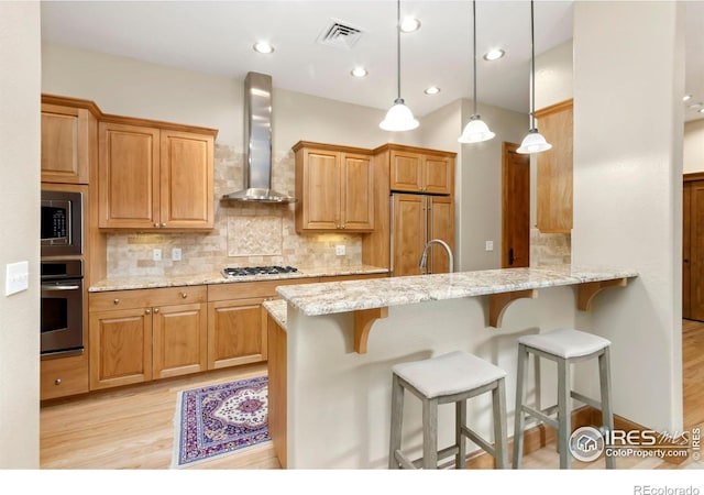 kitchen with built in appliances, hanging light fixtures, kitchen peninsula, wall chimney range hood, and light wood-type flooring