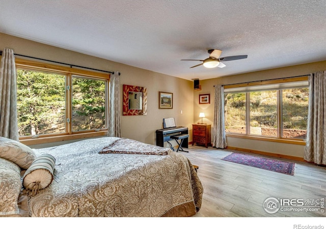 bedroom with multiple windows, ceiling fan, light hardwood / wood-style floors, and a textured ceiling