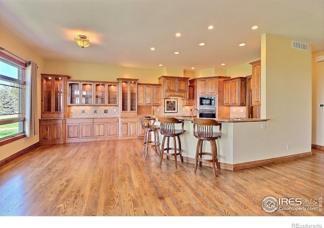 kitchen with appliances with stainless steel finishes, decorative backsplash, light stone countertops, light wood-type flooring, and a kitchen bar