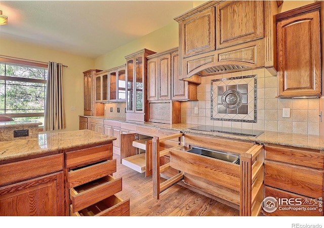 kitchen featuring decorative backsplash, light wood-type flooring, light stone counters, and black electric cooktop