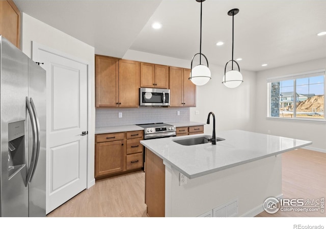 kitchen featuring sink, hanging light fixtures, light hardwood / wood-style floors, a kitchen island with sink, and appliances with stainless steel finishes