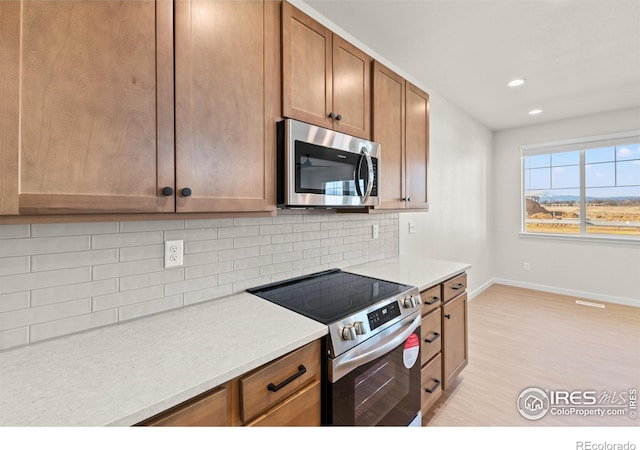 kitchen featuring backsplash, light stone countertops, light hardwood / wood-style flooring, and appliances with stainless steel finishes