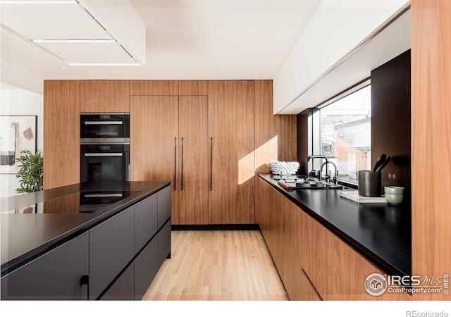 kitchen featuring double oven, sink, wooden walls, and light hardwood / wood-style floors