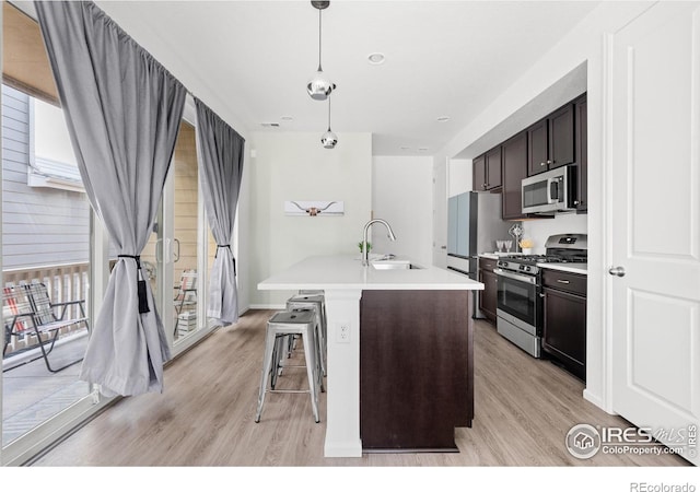 kitchen with a center island with sink, sink, hanging light fixtures, light hardwood / wood-style floors, and stainless steel appliances