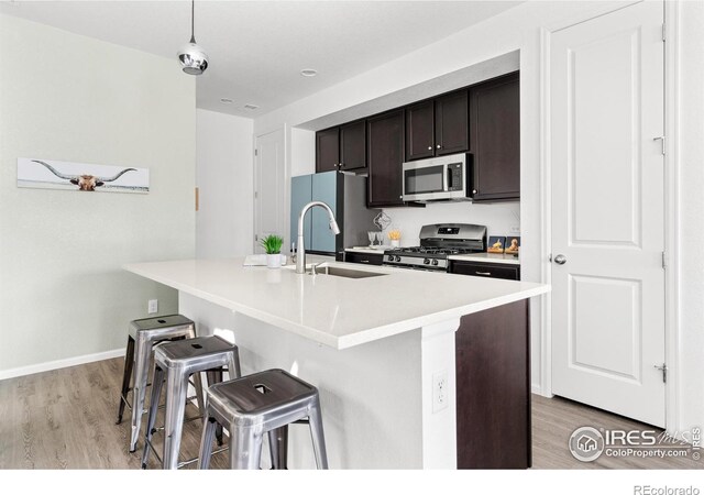 kitchen featuring appliances with stainless steel finishes, a kitchen breakfast bar, dark brown cabinetry, light hardwood / wood-style floors, and hanging light fixtures