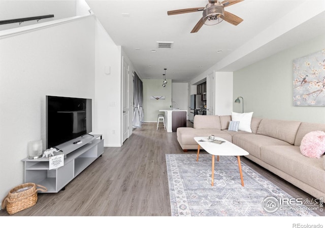 living room with ceiling fan, light wood-type flooring, and sink