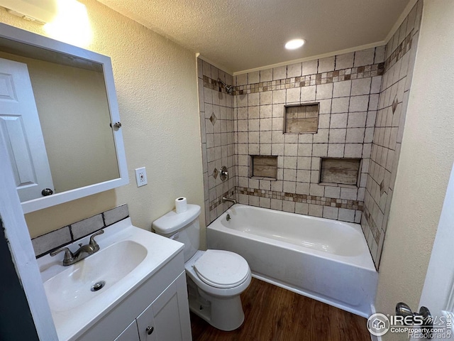 full bathroom featuring a textured ceiling, hardwood / wood-style flooring, tiled shower / bath, vanity, and toilet