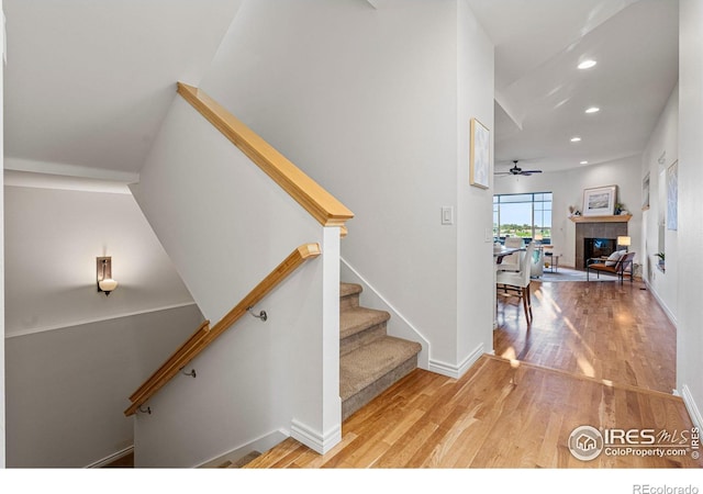 stairs featuring ceiling fan, hardwood / wood-style flooring, and a tile fireplace