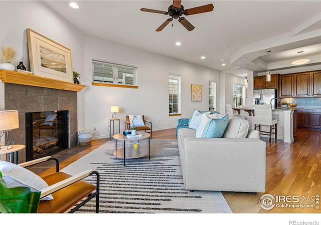 living room with light wood-type flooring, a tile fireplace, sink, and ceiling fan